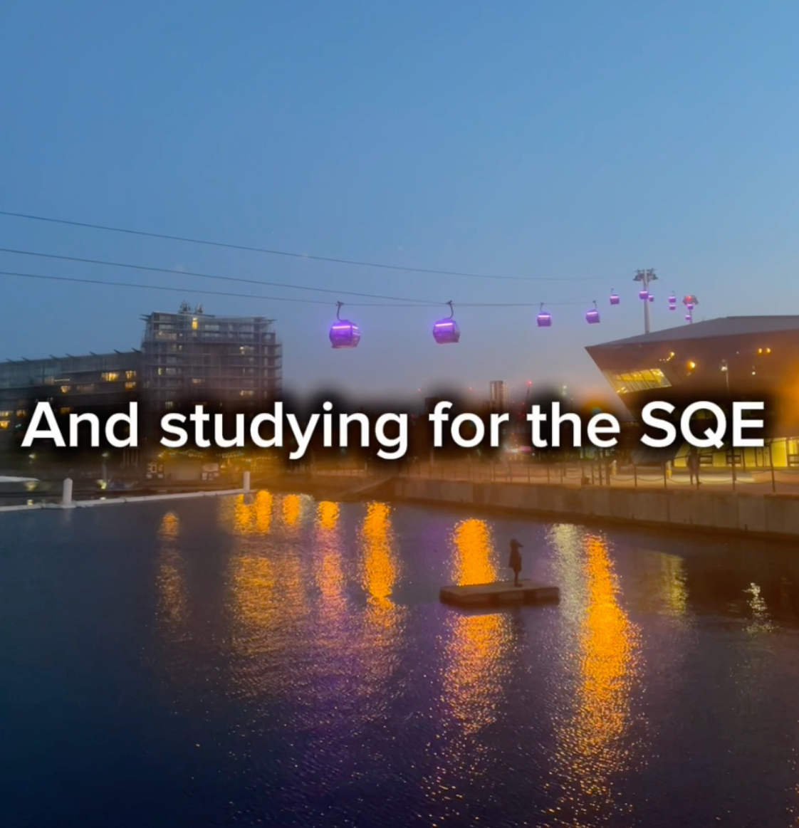 This is a thumbnail for a video that includes the evening cityscape showing a waterfront scene with illuminated purple cable car gondolas crossing overhead against a dusky blue sky. The image features a modern building with warm lighting reflected in the water below, with a small boat visible on the water. Large white text overlay reads 'And studying for the SQE'. This image is from a learner on the SQE apprenticeship who will be discussing the programme and the inclusion of the the Solicitors Qualifying Examination while balancing work and life commitments.